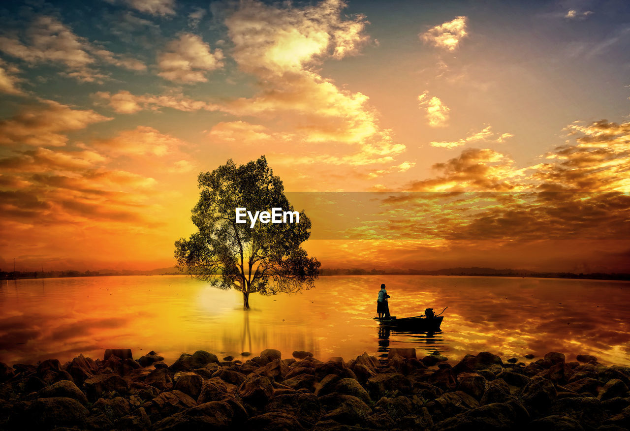 SILHOUETTE OF MAN SITTING ON SHORE AGAINST SUNSET SKY