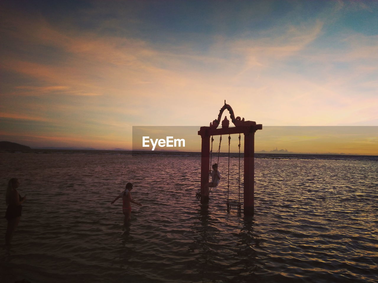 SILHOUETTE WOODEN POST IN SEA AGAINST SKY AT SUNSET