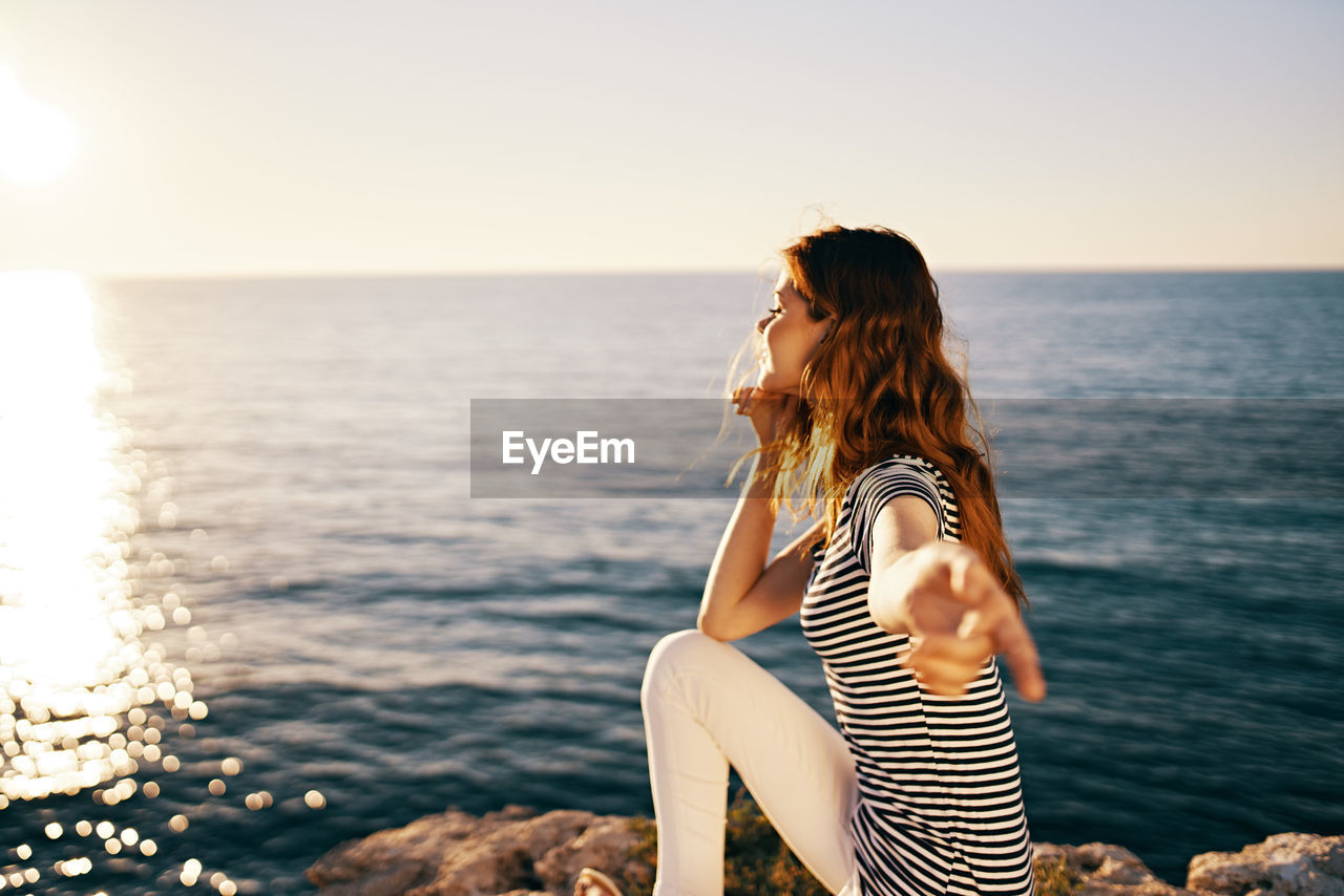 Woman sitting by sea against sky