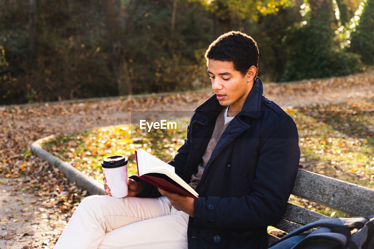 Full length of man reading book sitting at bench at park