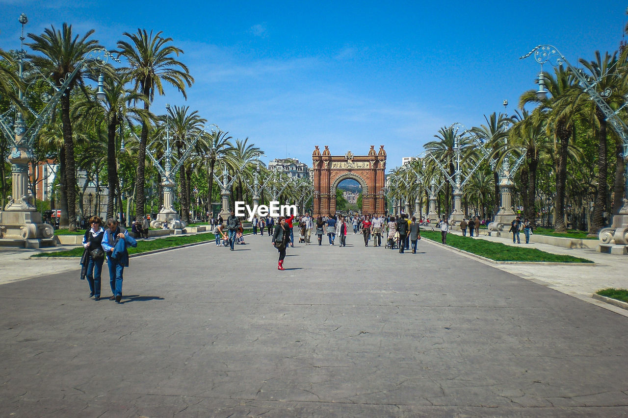 Group of people walking in front of palm trees, arc de triomf barcelona 
