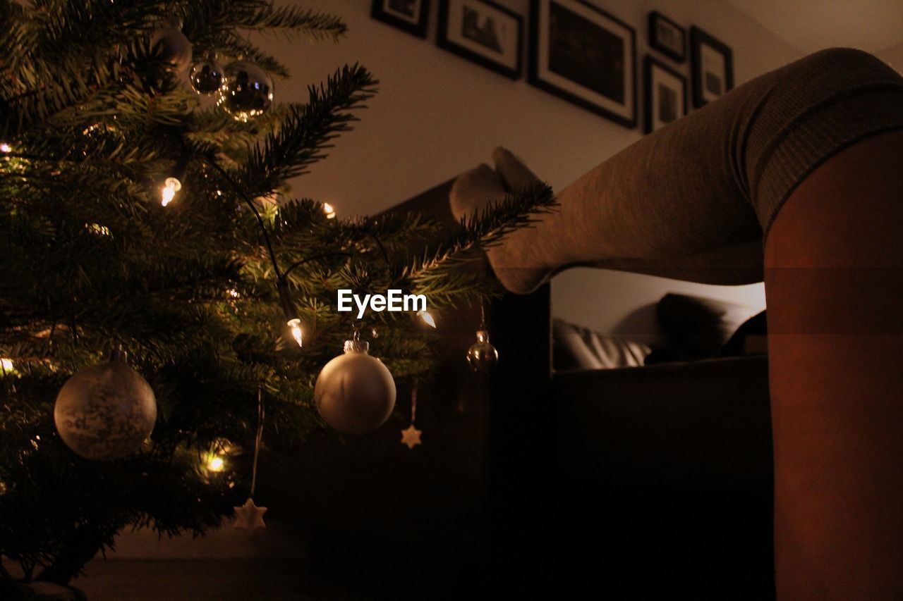 Low section of woman by illuminated christmas tree at home