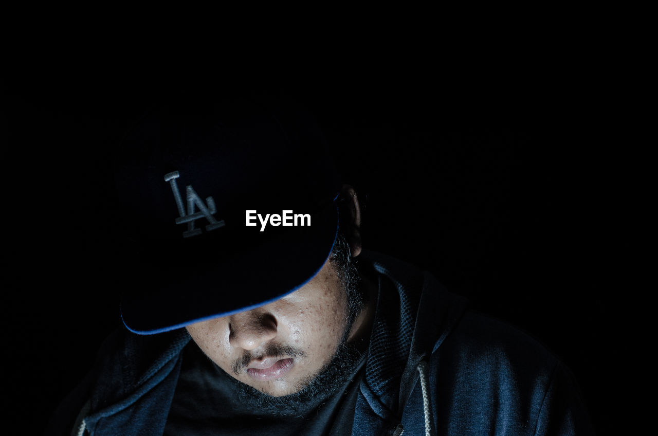 Close-up of man wearing cap against black background