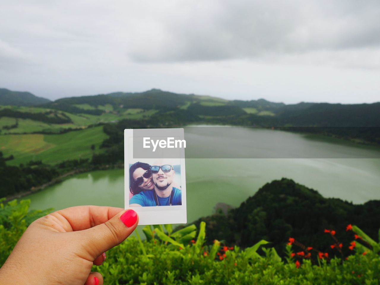 Cropped image of woman hand holding instant print transfer against lake