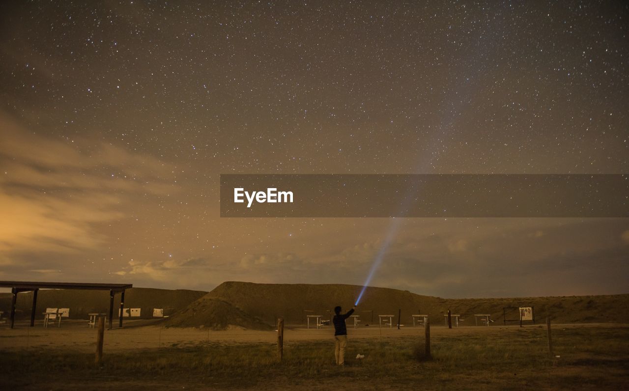 Rear view of man lighting flashlight star field in sky