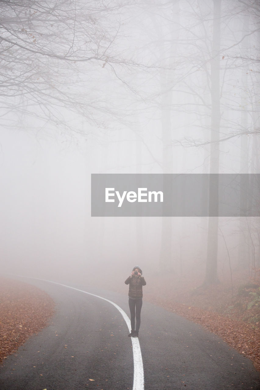 Full length of woman photographing with camera while standing on road in foggy weather