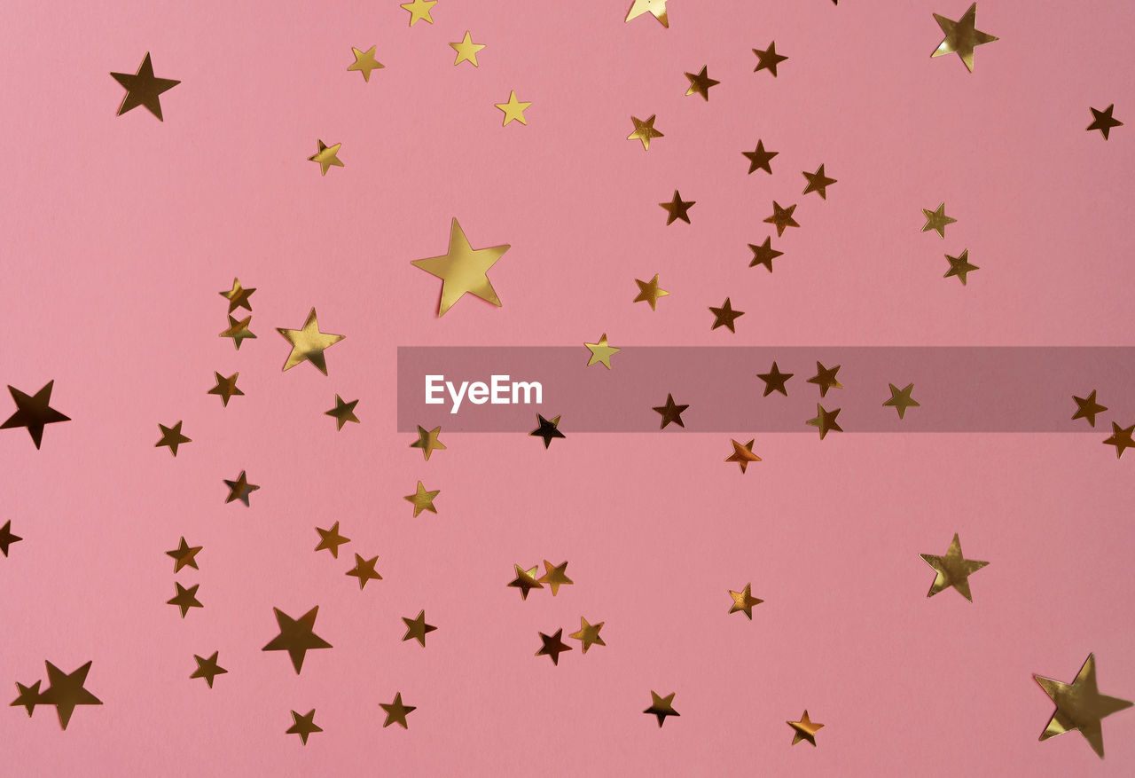 Golden stars glittering confetti on pink background. trendy festive holiday backdrop.