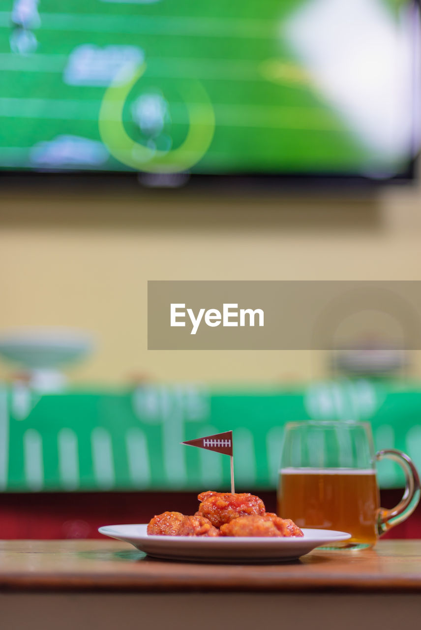 Plate of spicy boneless wings and large glass mug of beer in front of tv watching football game