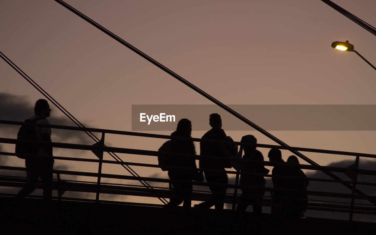 Silhouette people standing on bridge against sky during sunset