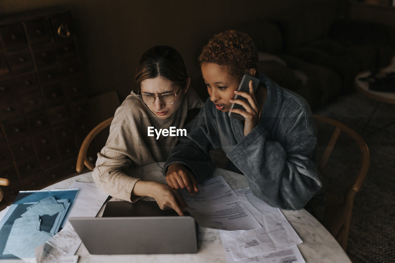 High angle view of non-binary couple doing finance on laptop at home