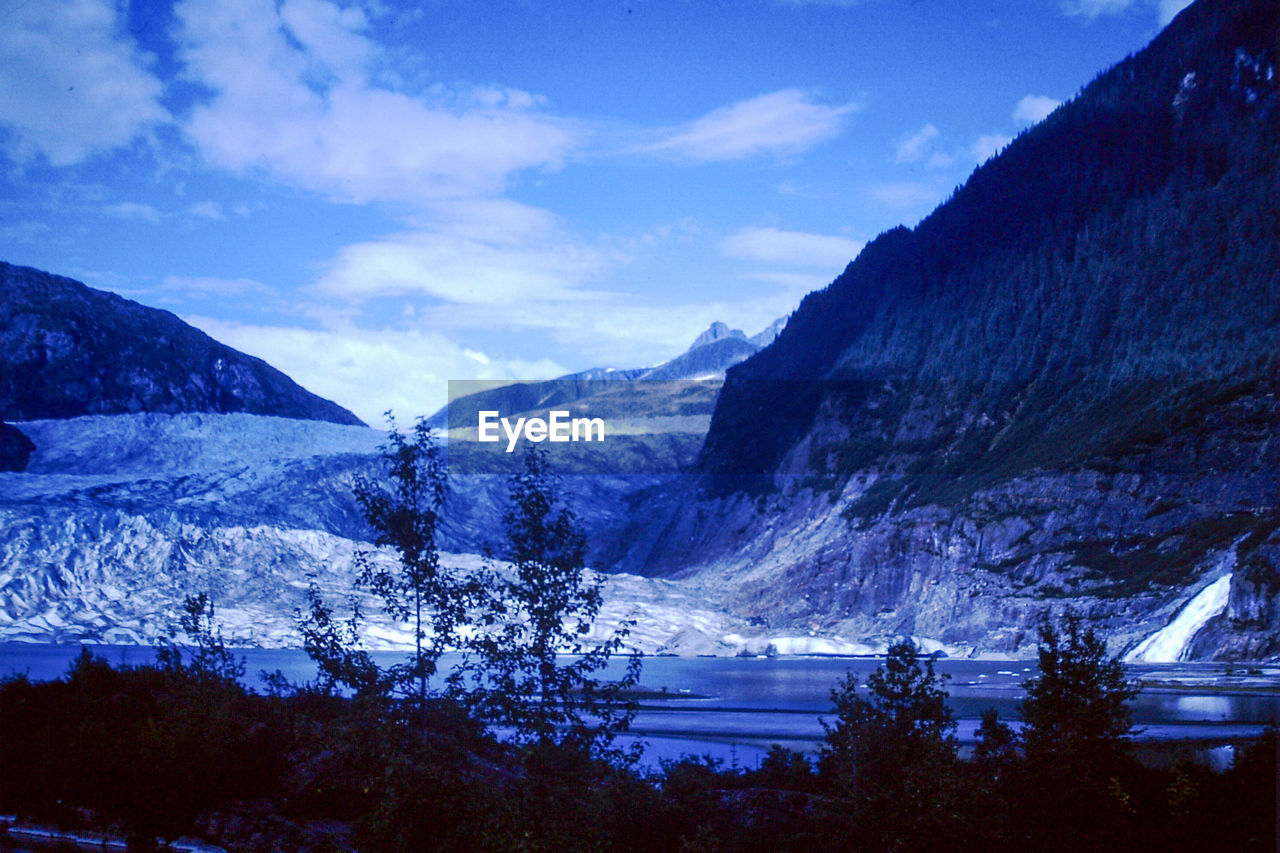mountain, snow, scenics - nature, cold temperature, winter, beauty in nature, environment, sky, mountain range, landscape, cloud, nature, tree, plant, tranquil scene, no people, tranquility, snowcapped mountain, land, blue, non-urban scene, travel destinations, pinaceae, coniferous tree, pine tree, forest, travel, outdoors, wilderness, water, idyllic, frozen