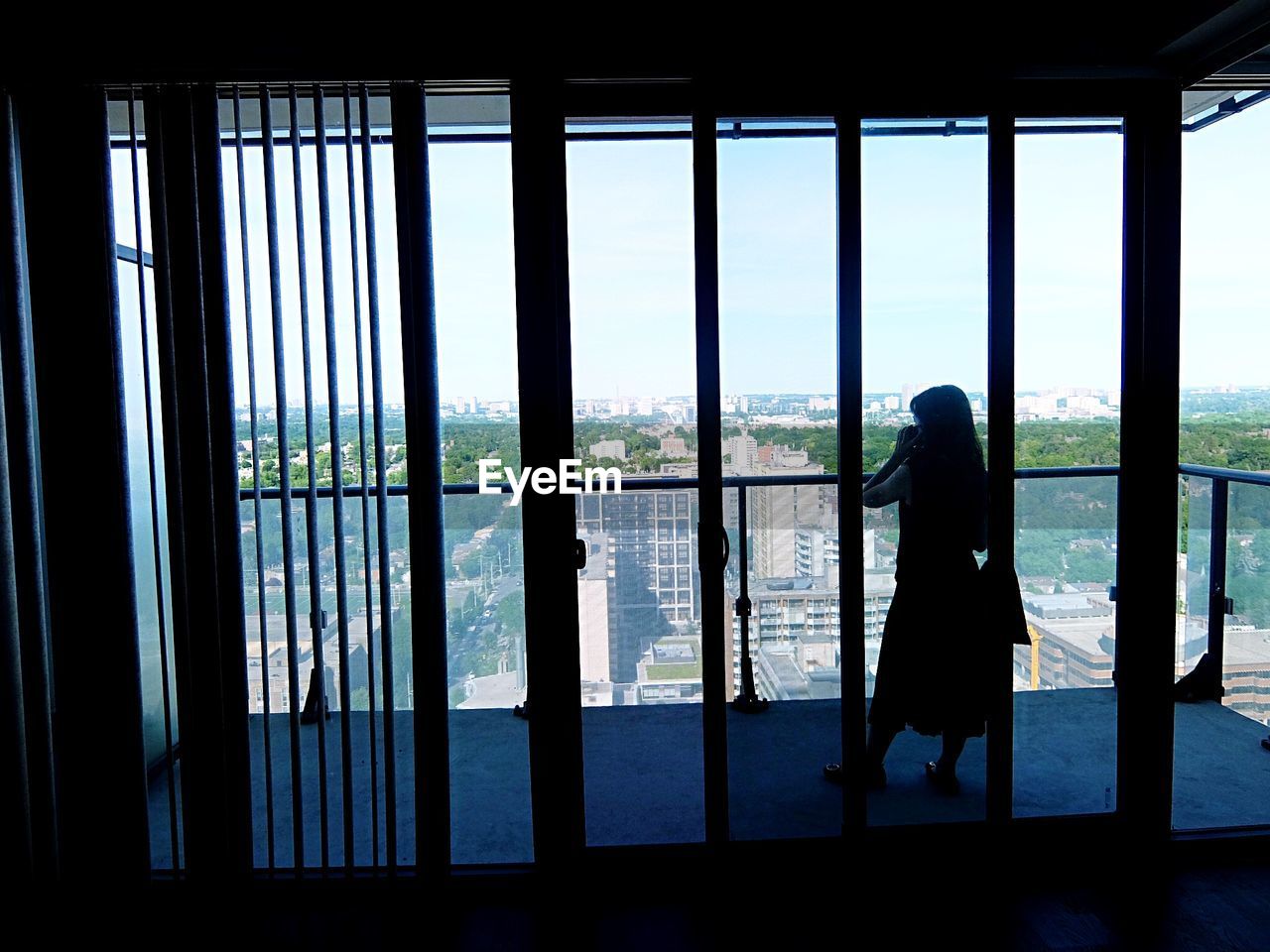 REAR VIEW OF WOMAN LOOKING THROUGH WINDOW IN GLASS