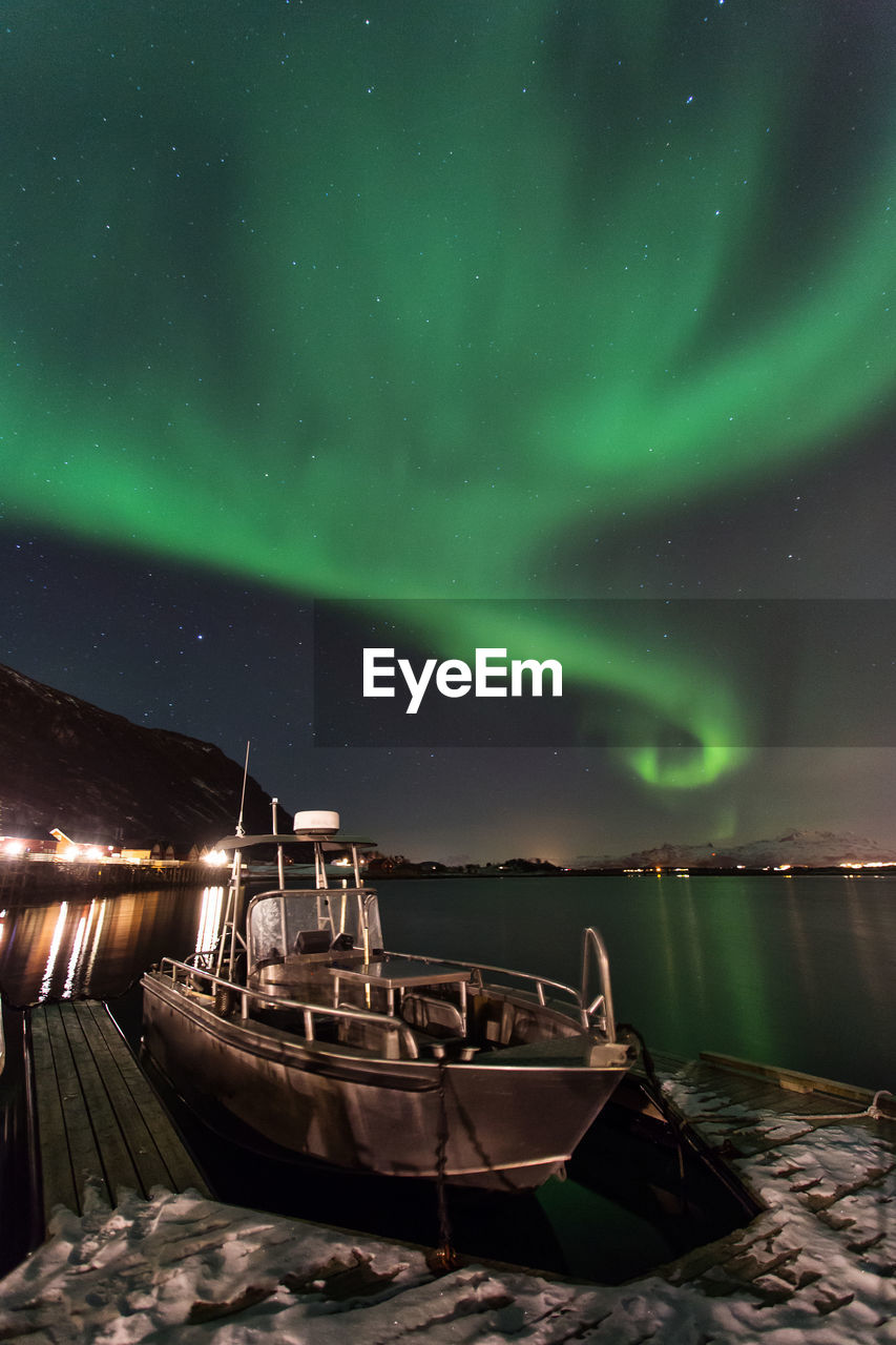 BOAT MOORED AT ILLUMINATED LAKE AGAINST SKY AT NIGHT
