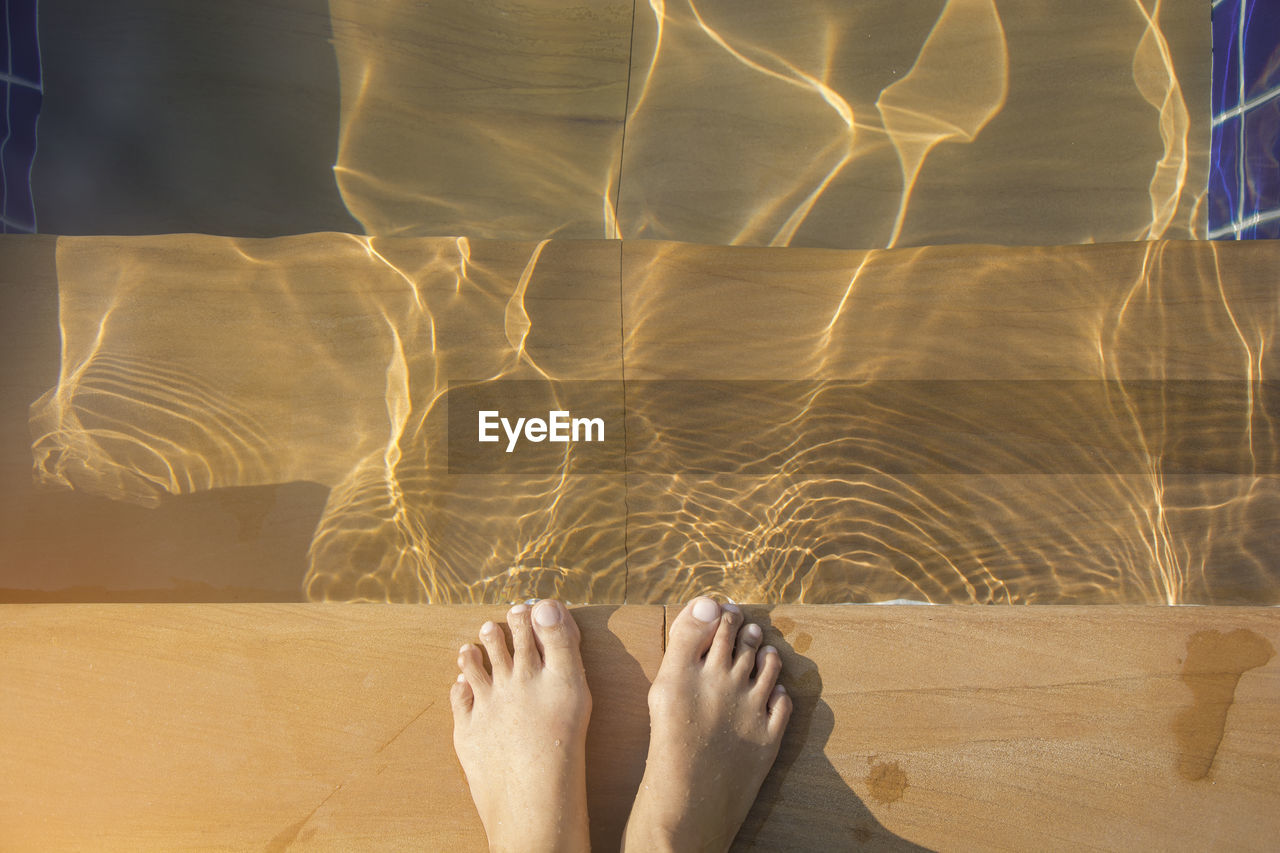 LOW SECTION OF WOMAN STANDING ON WATER AT BEACH