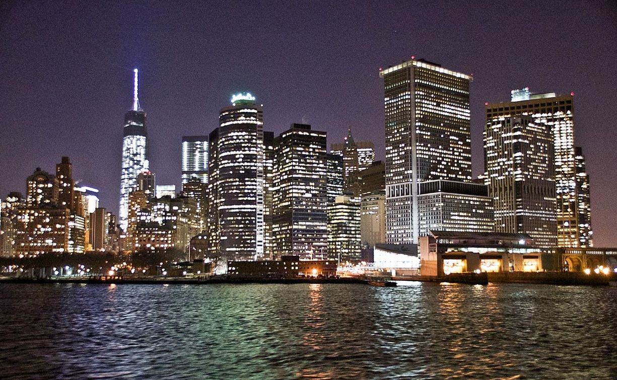 River in front of illuminated modern buildings against sky at night