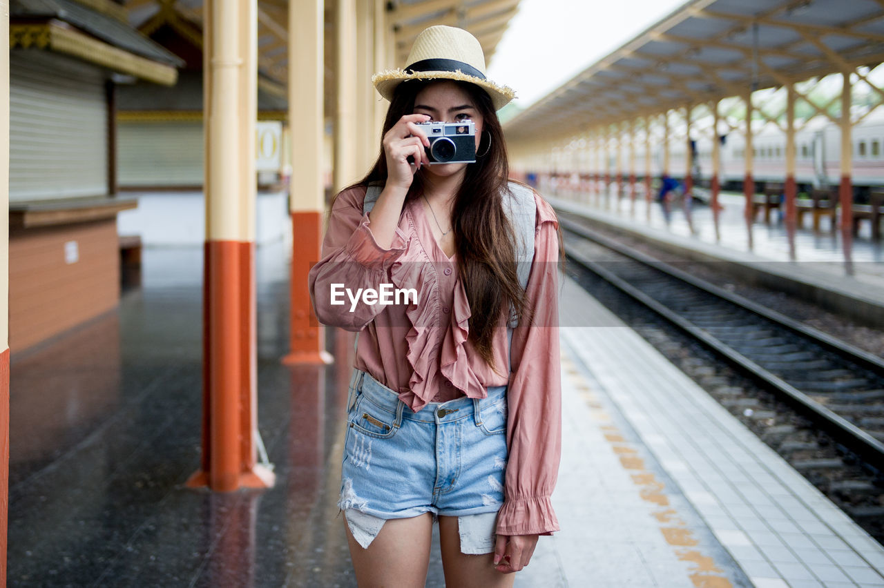 Woman photographing while standing at railroad station platform