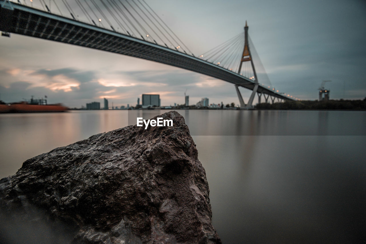 Low angle view of bridge over river in city against cloudy sky