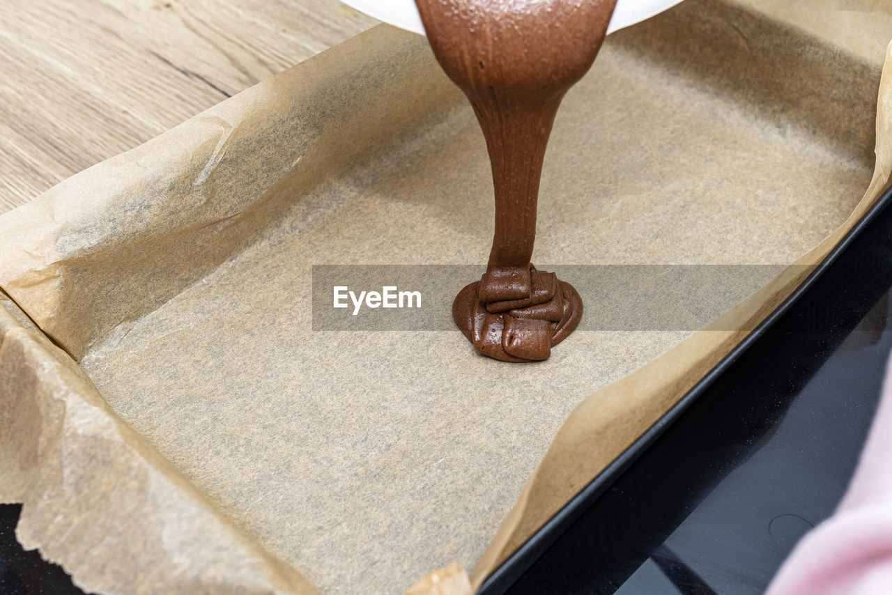 Pouring a liquid thick mass of cocoa dough onto a baking sheet lined with baking paper.