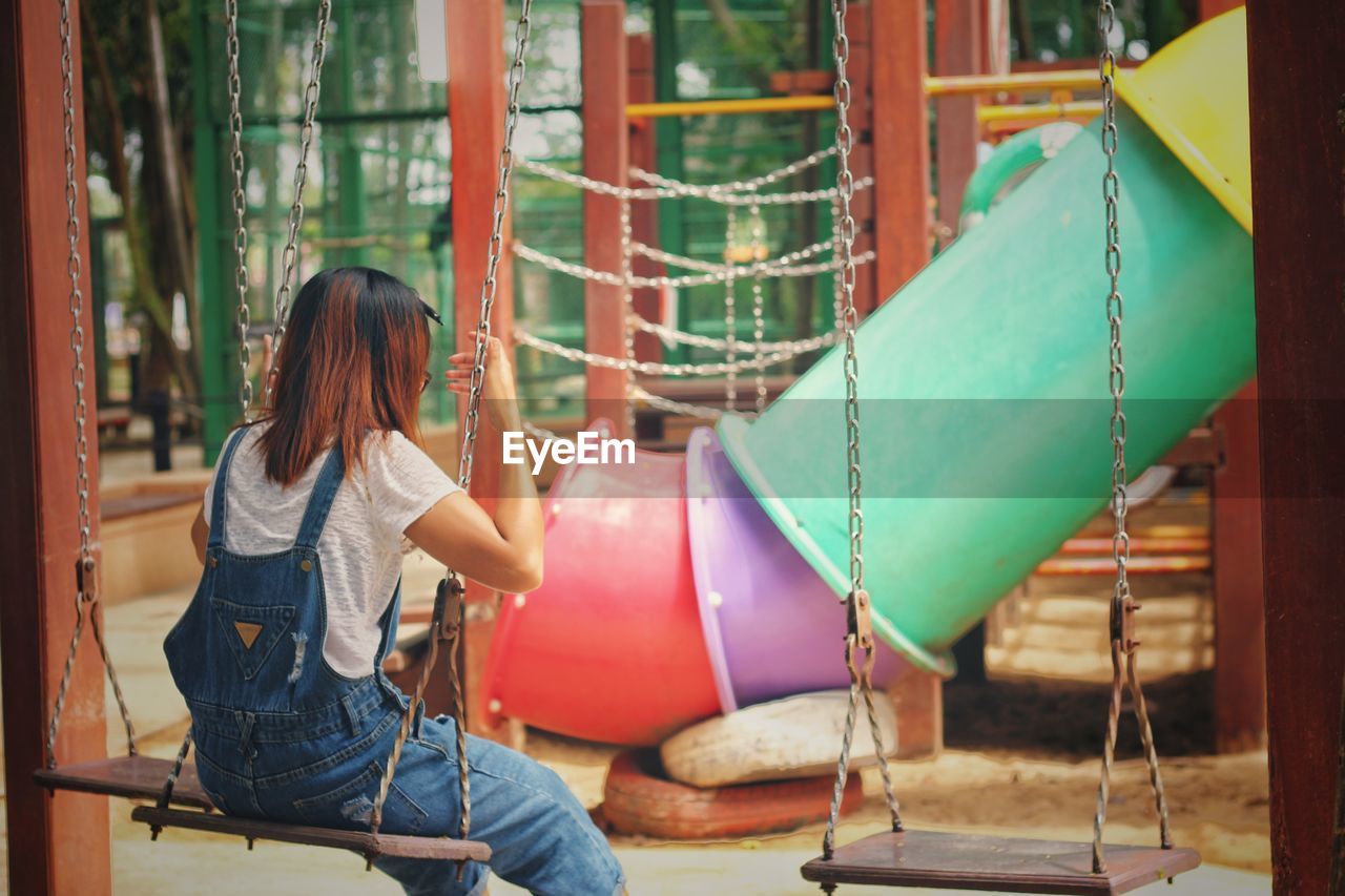 Rear view of woman sitting on swing in playground