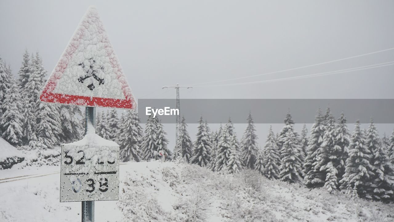 Road sign on snow covered landscape against sky