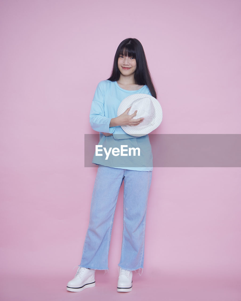 PORTRAIT OF YOUNG WOMAN STANDING AGAINST PINK WALL