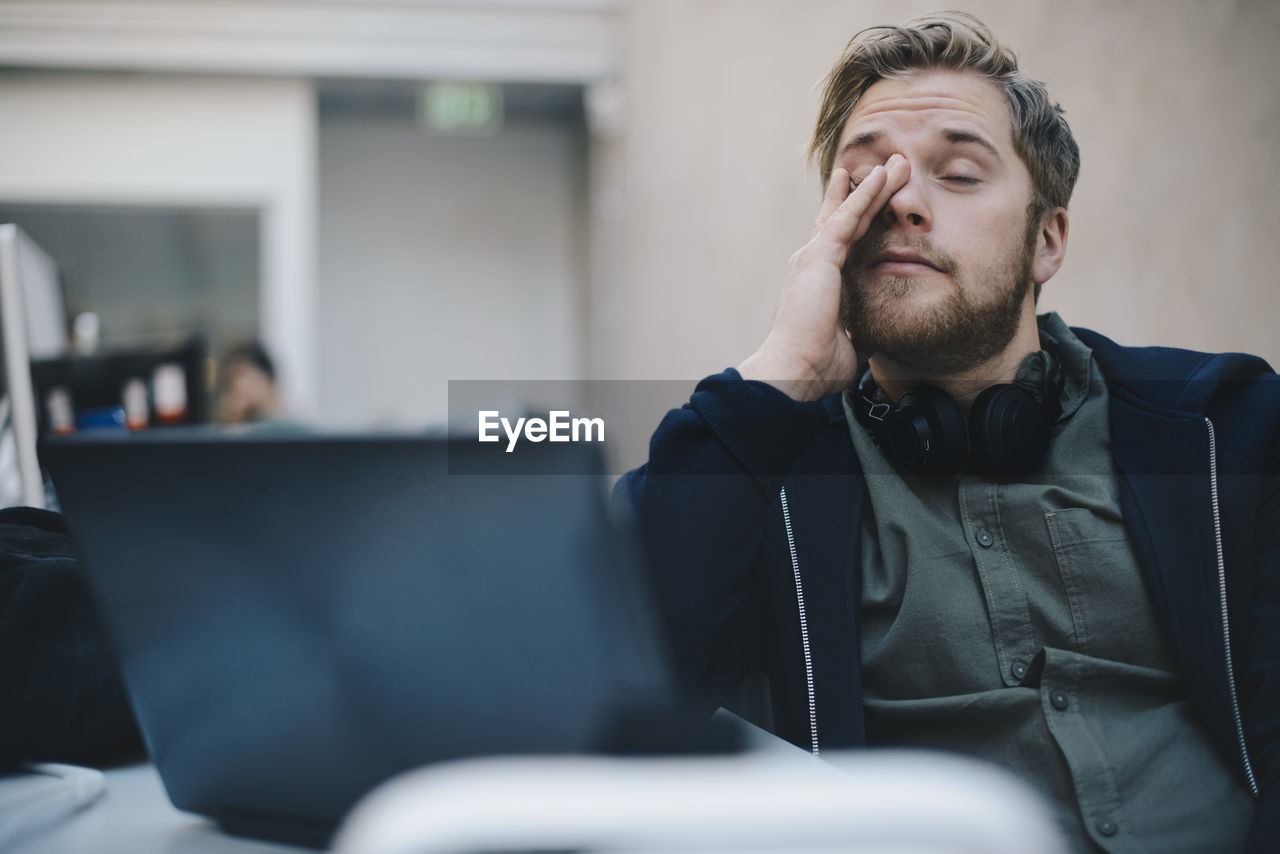 Tired computer programmer rubbing eyes while sitting in office