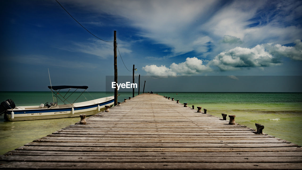 Empty jetty leading to pier over sea against sky