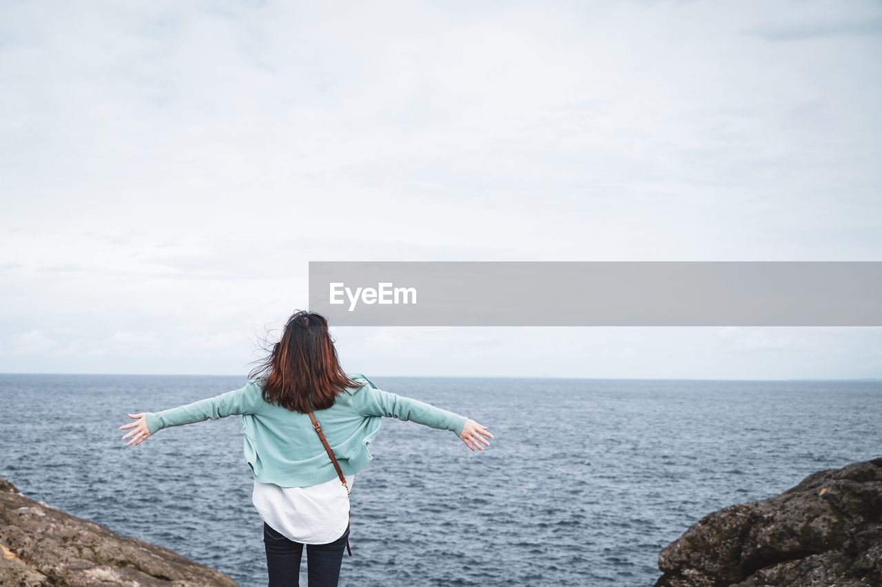 REAR VIEW OF WOMAN LOOKING AT SEA