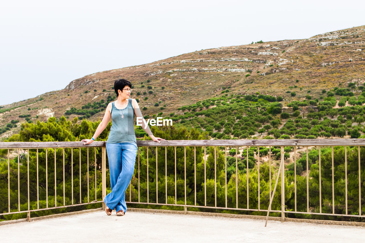 MAN STANDING ON RAILING AGAINST MOUNTAIN