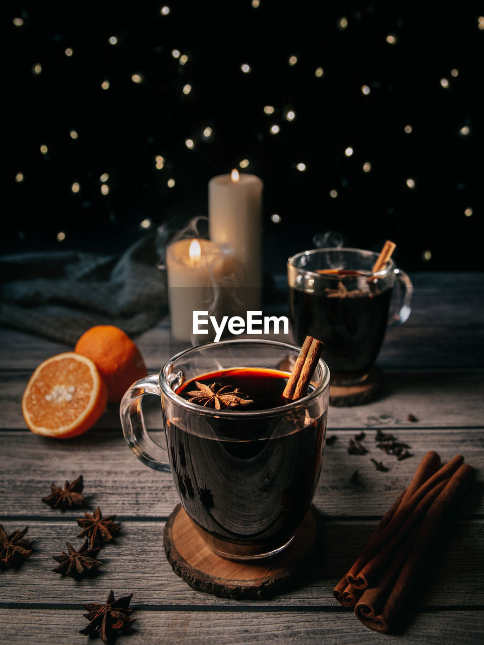 Still life of mugs filled with mulled wine at night on wooden table with spices and candles