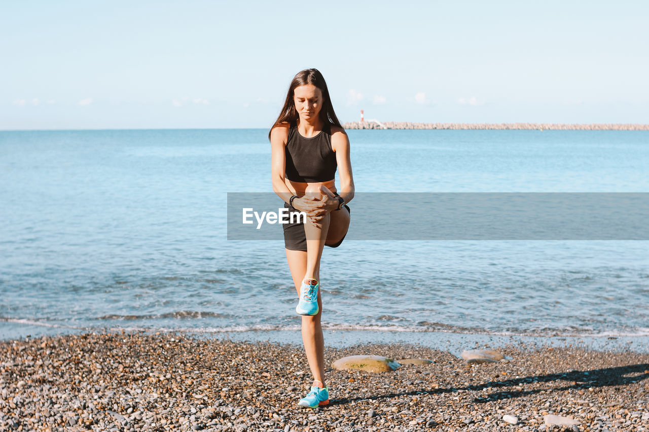 Woman exercising at beach against sky