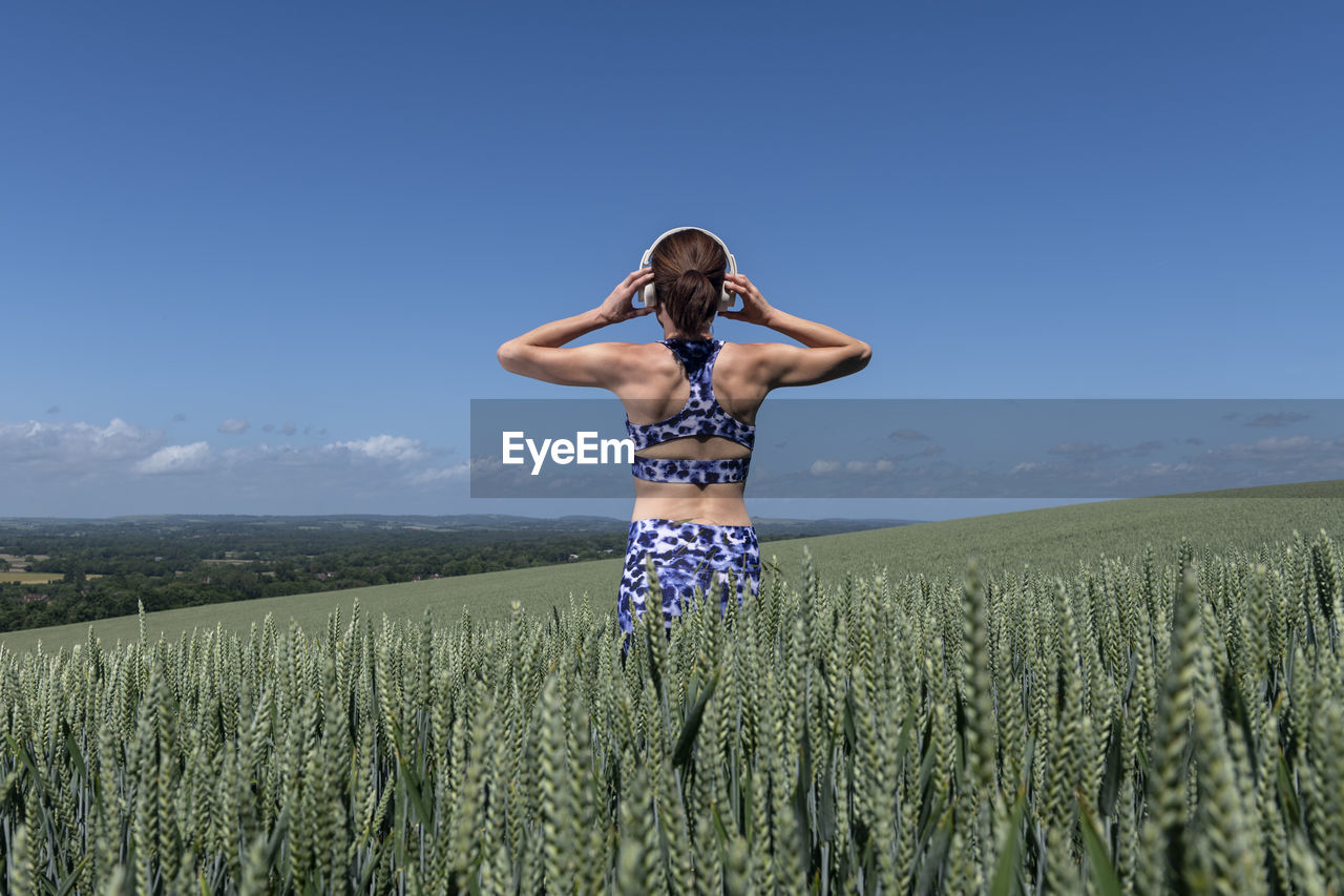 Sporty, fit woman listening to music with wireless headphones in a field.rear view