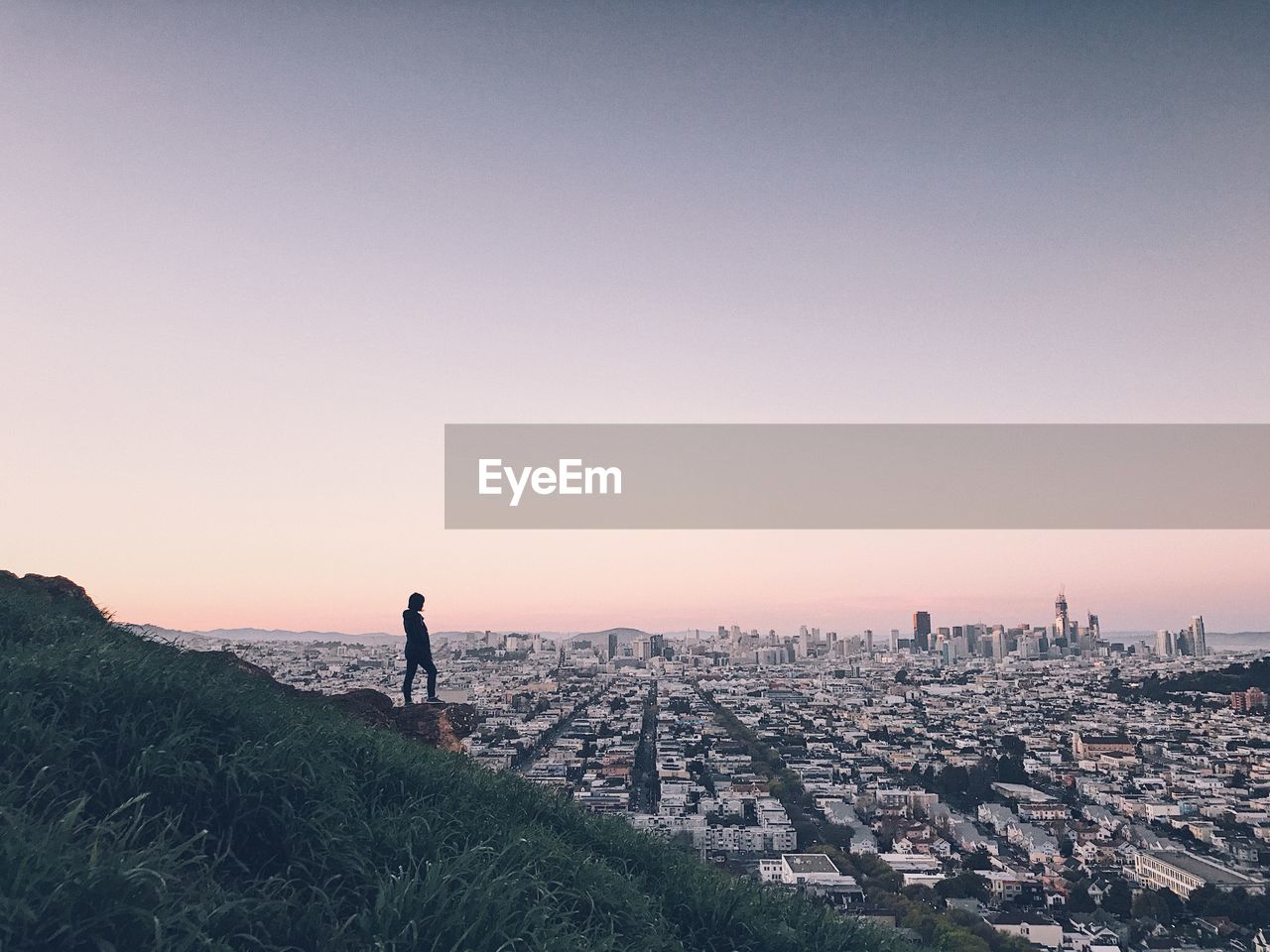 Woman standing on mountain overlooking cityscape against sky during sunset