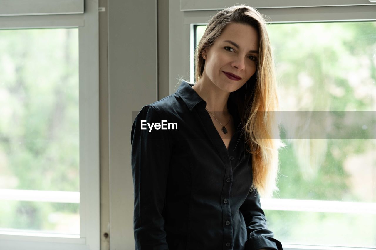 Portrait of beautiful young woman standing against window