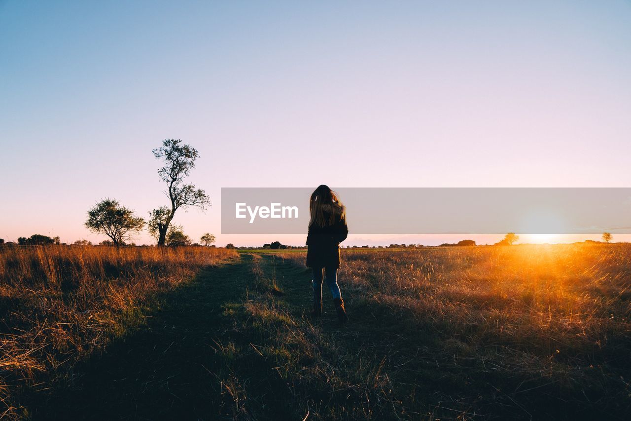 Woman standing on field against clear sky during sunset