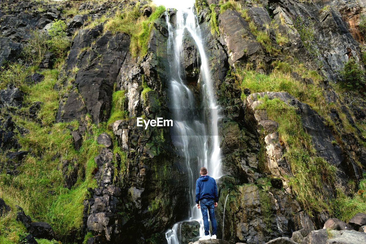 Rear view full length of man standing against waterfall