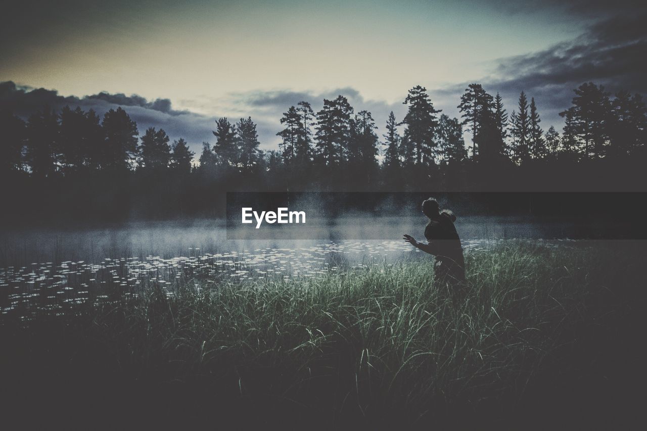 Silhouette of man standing in meadow and looking at river 