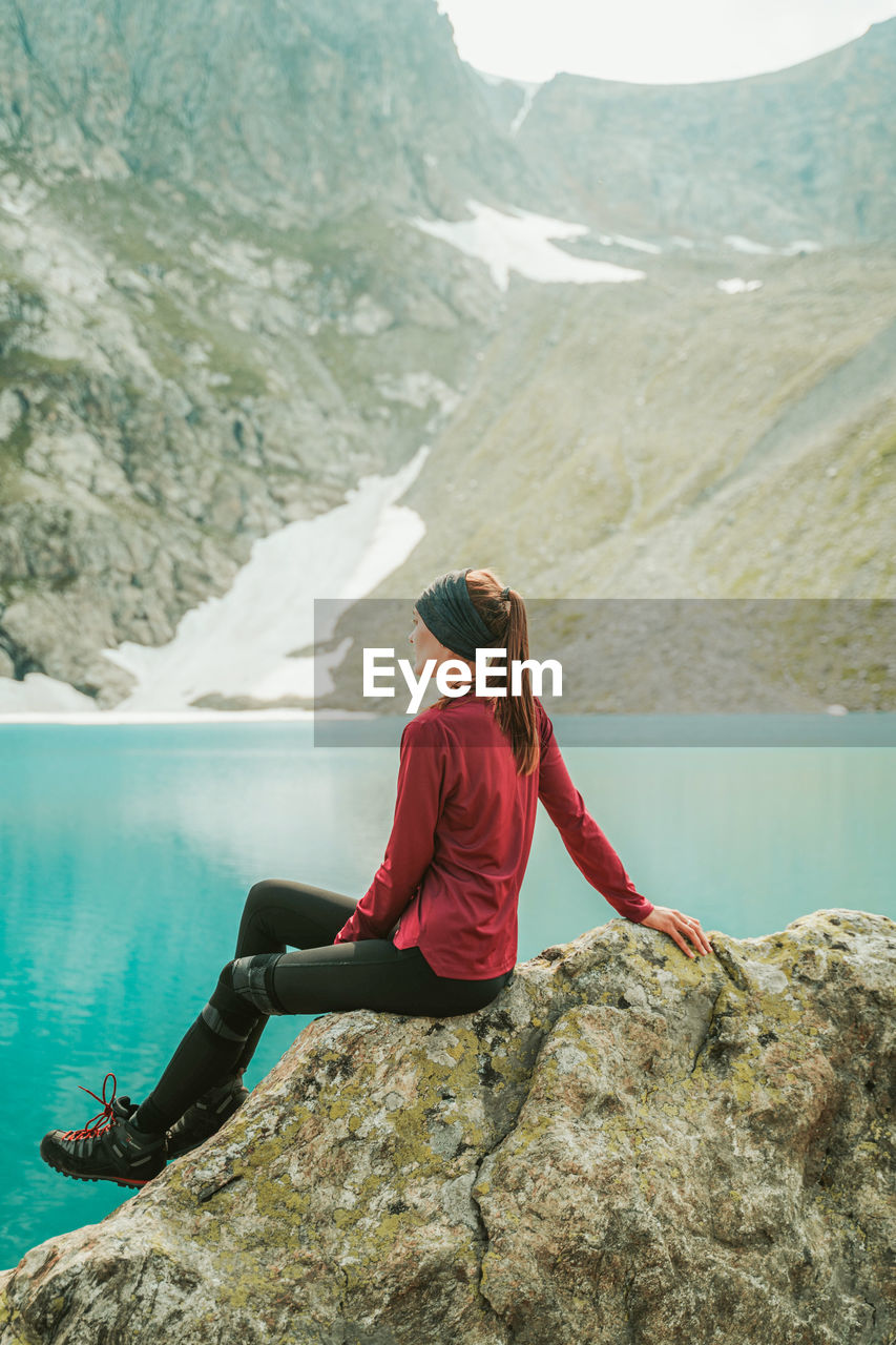 WOMAN SITTING ON ROCK BY MOUNTAIN