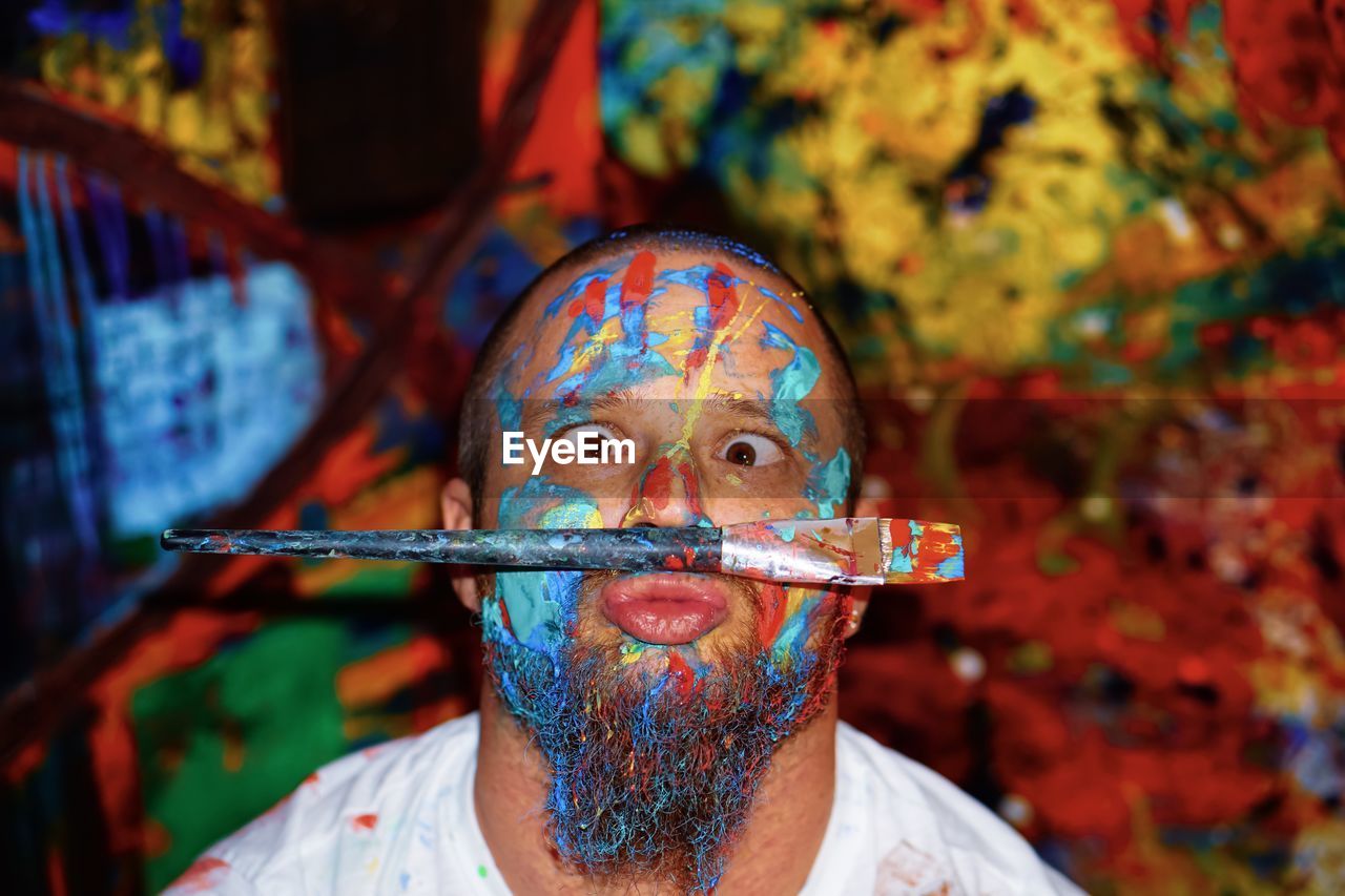 Portrait of funny man with messy painted face and paintbrush