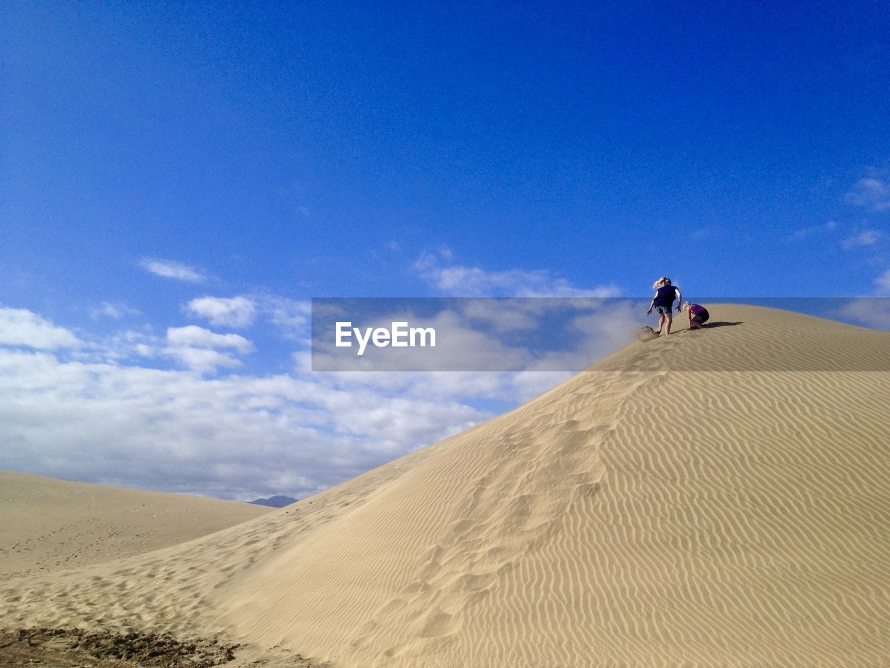 Low angle view of mother and son on sand dune in desert against blue sky