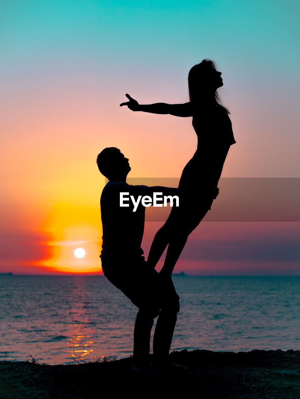 Silhouette couple exercising at beach against sky during sunset