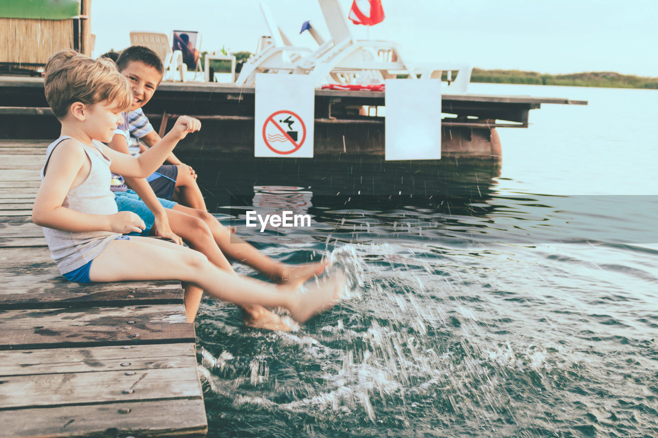 Playful kids having fun while sitting on a pier and splashing water.