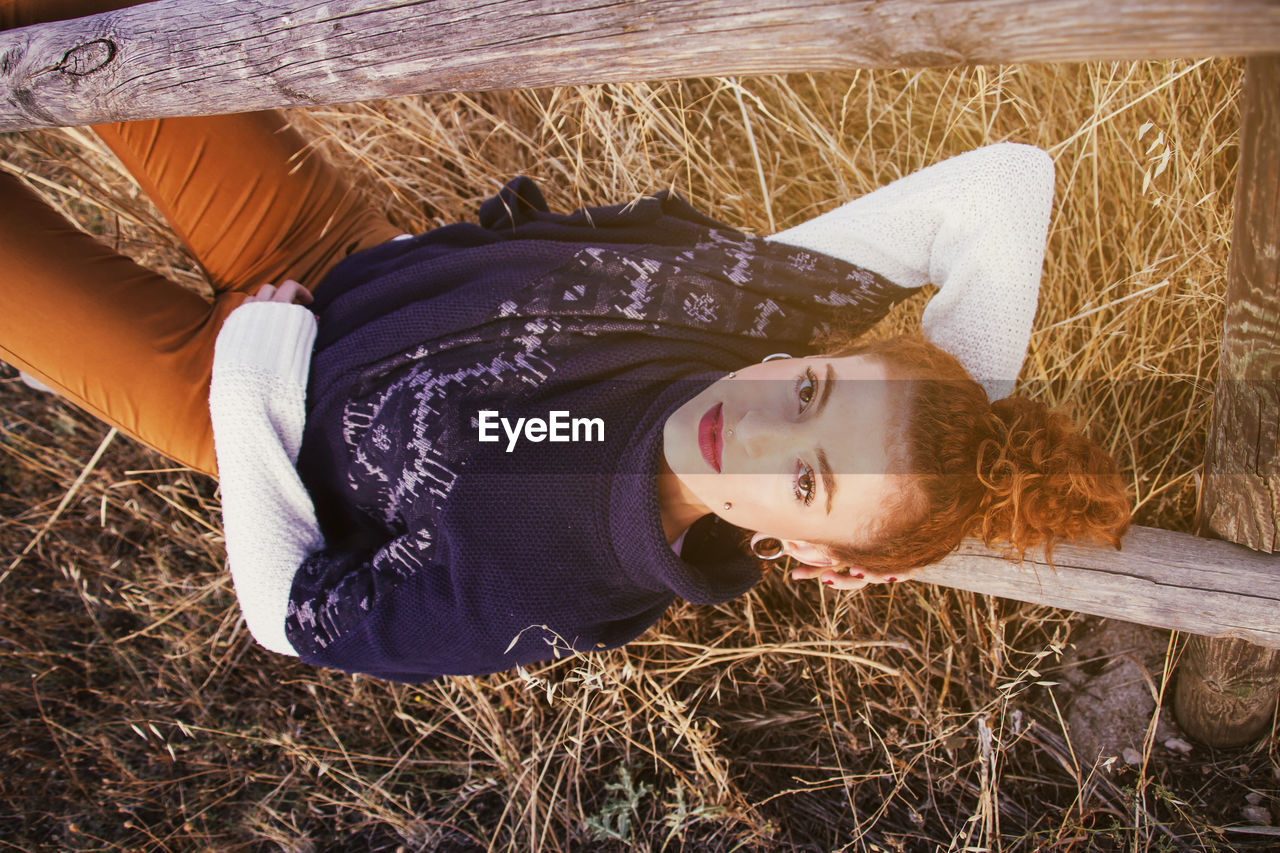 Portrait of young woman lying on railing at field