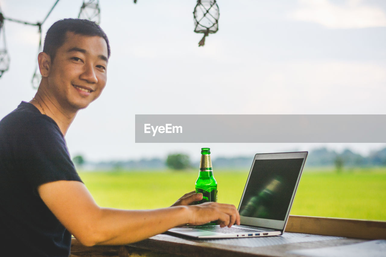 Portrait of man using laptop by field