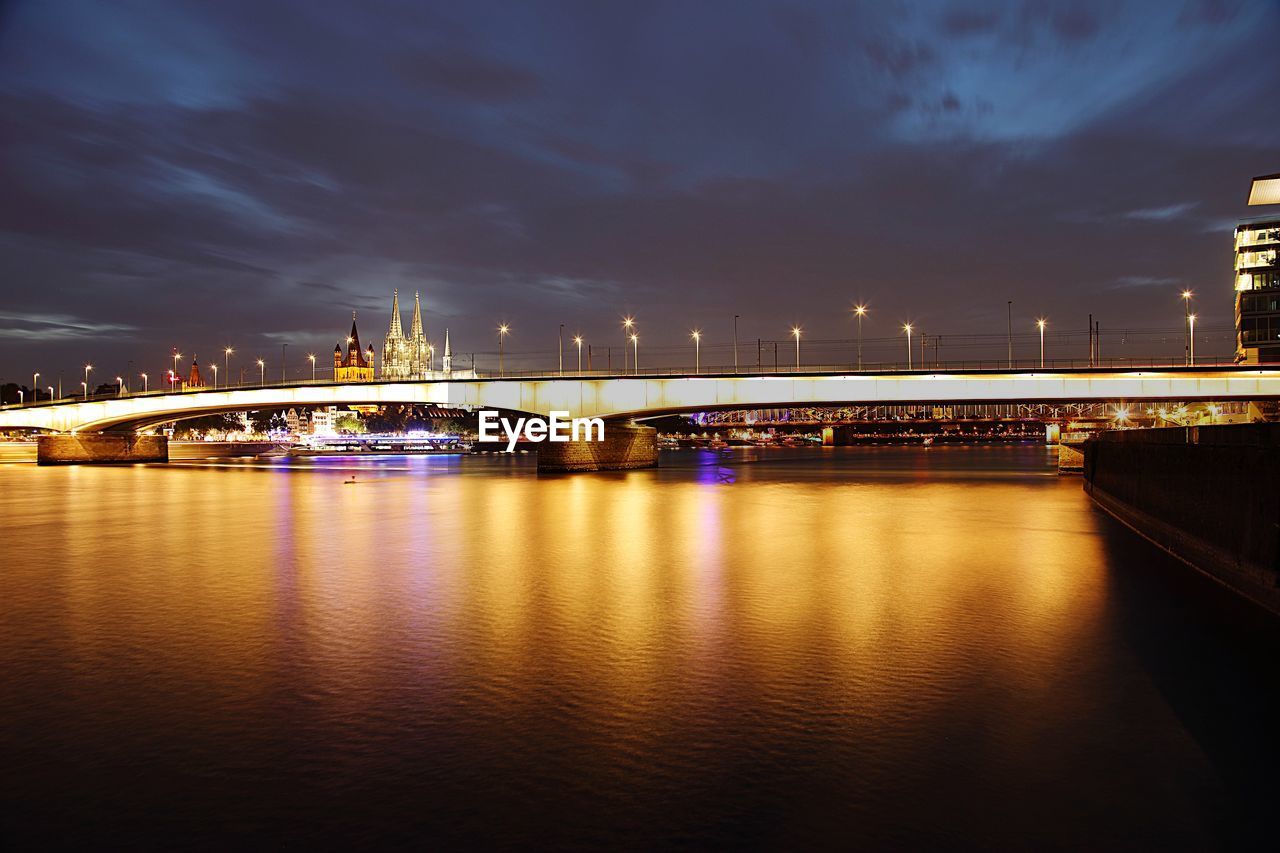 Illuminated bridge over river against sky in city at night