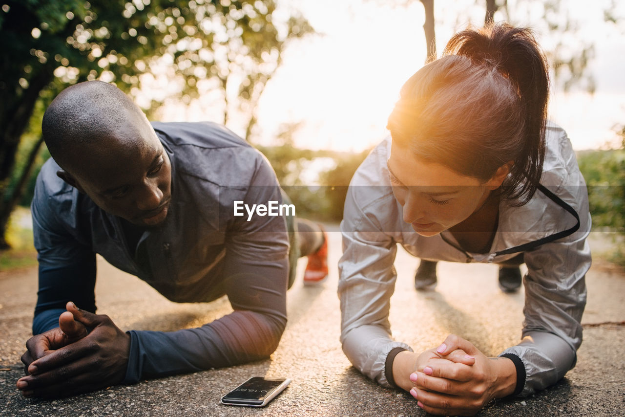 Male and female athletes looking at mobile phone while doing planks on road in park