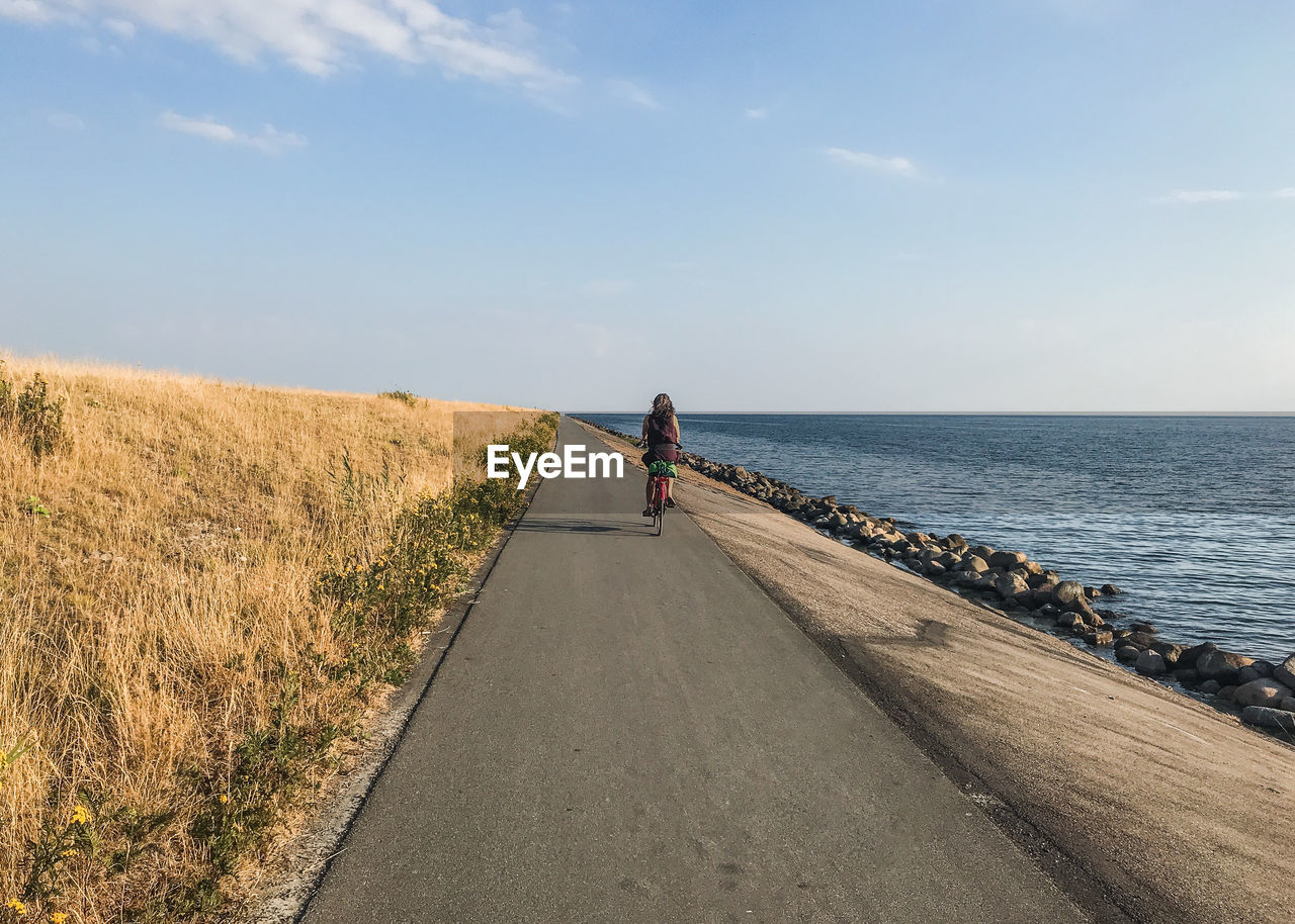 Rear view of woman riding bicycle on road by sea