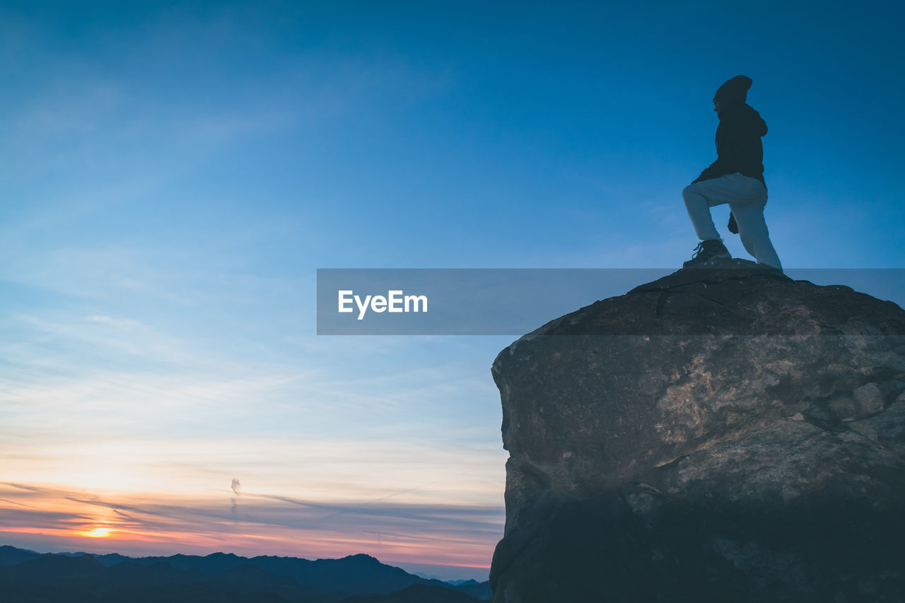 Low angle view of man standing on rock against sky