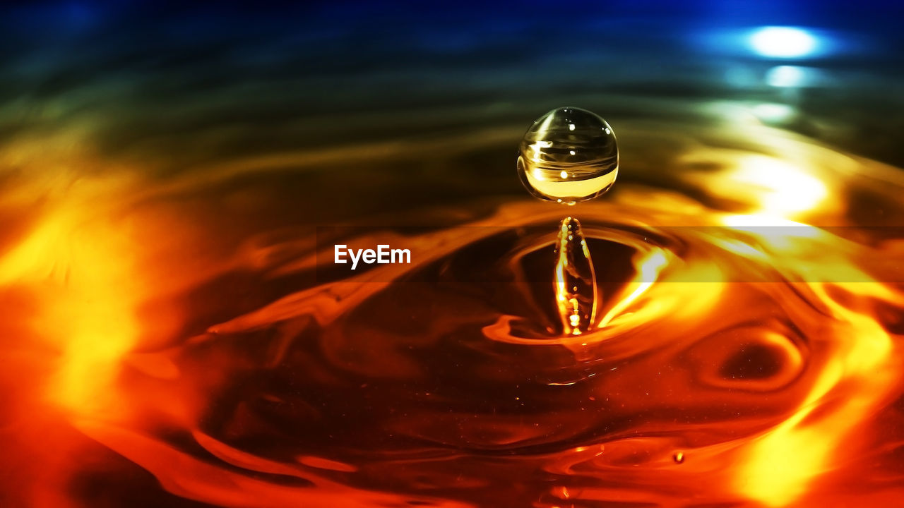 CLOSE-UP OF WATER DROP ON GLASS AGAINST ORANGE BACKGROUND