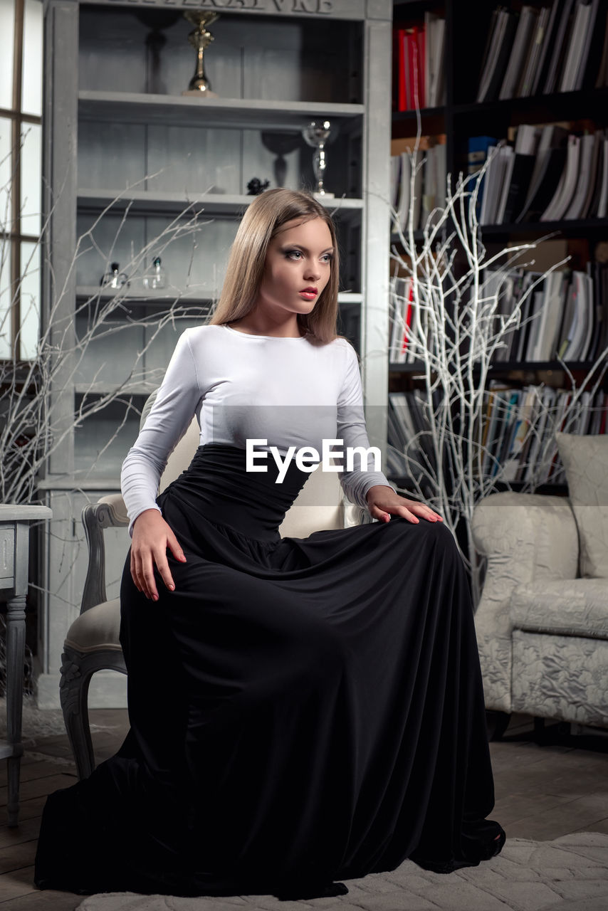 Confident woman wearing dress while sitting on chair at home